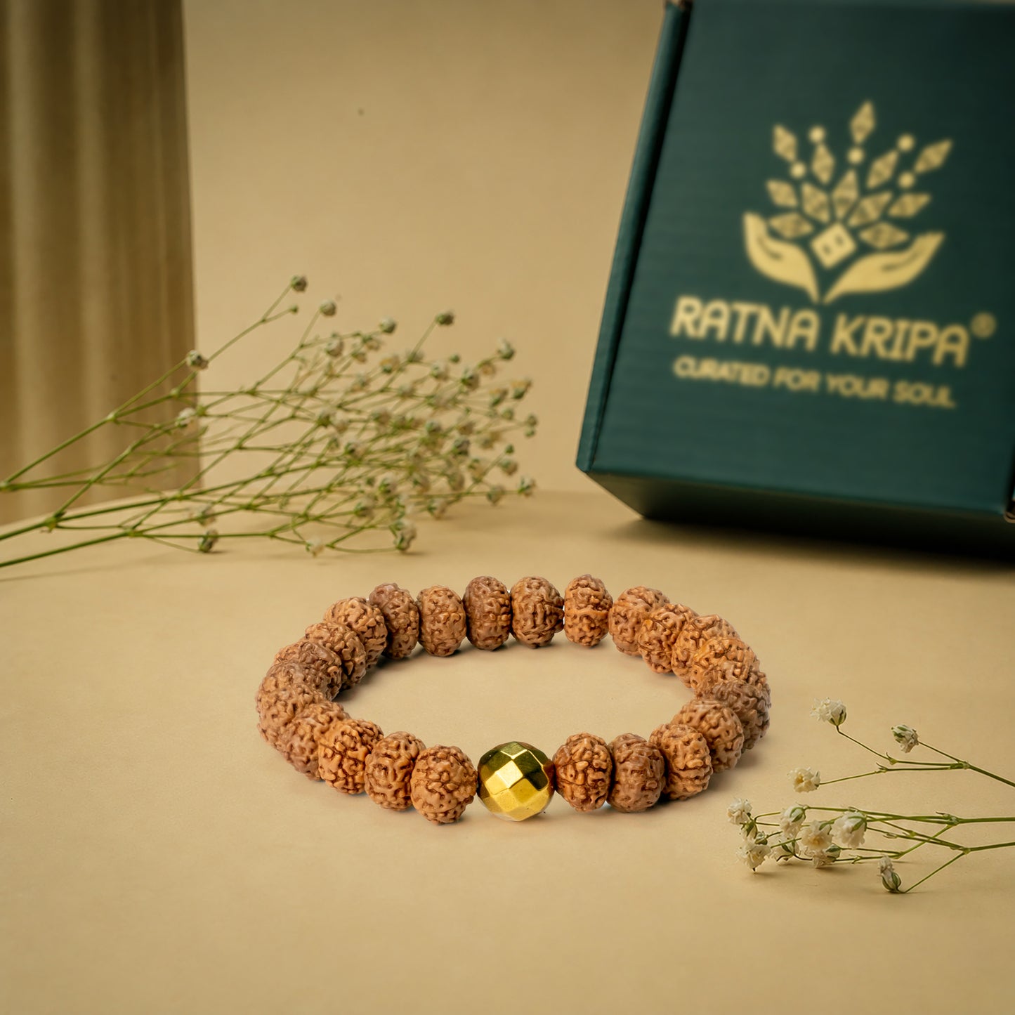 Bracelet with golden hematite bead on a beige surface next to a 'Ratna Kripa' box.