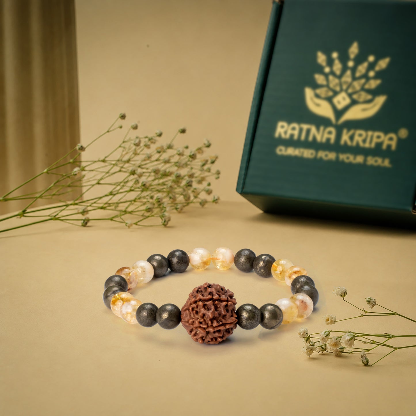 Bracelet with beads on a beige surface next to a green box with 'Ratna Kripa' branding.