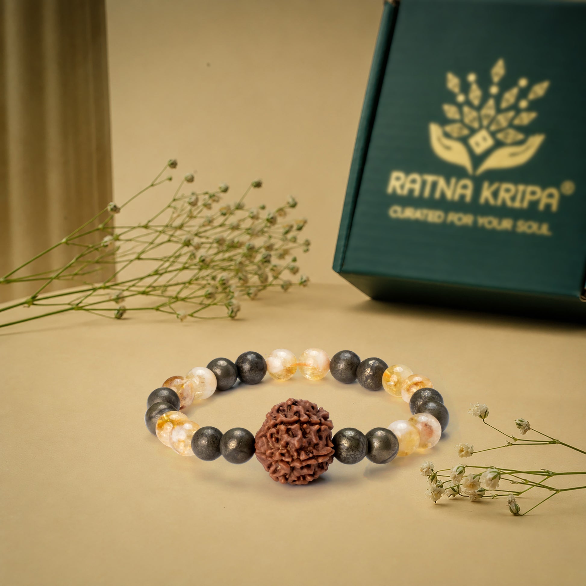 Bracelet with beads on a beige surface next to a green box with 'Ratna Kripa' branding.