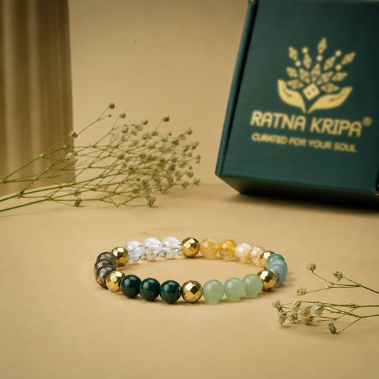Beaded bracelet with green, gold, and clear beads on a beige surface with a 'Ratna Kripa' box in the background.