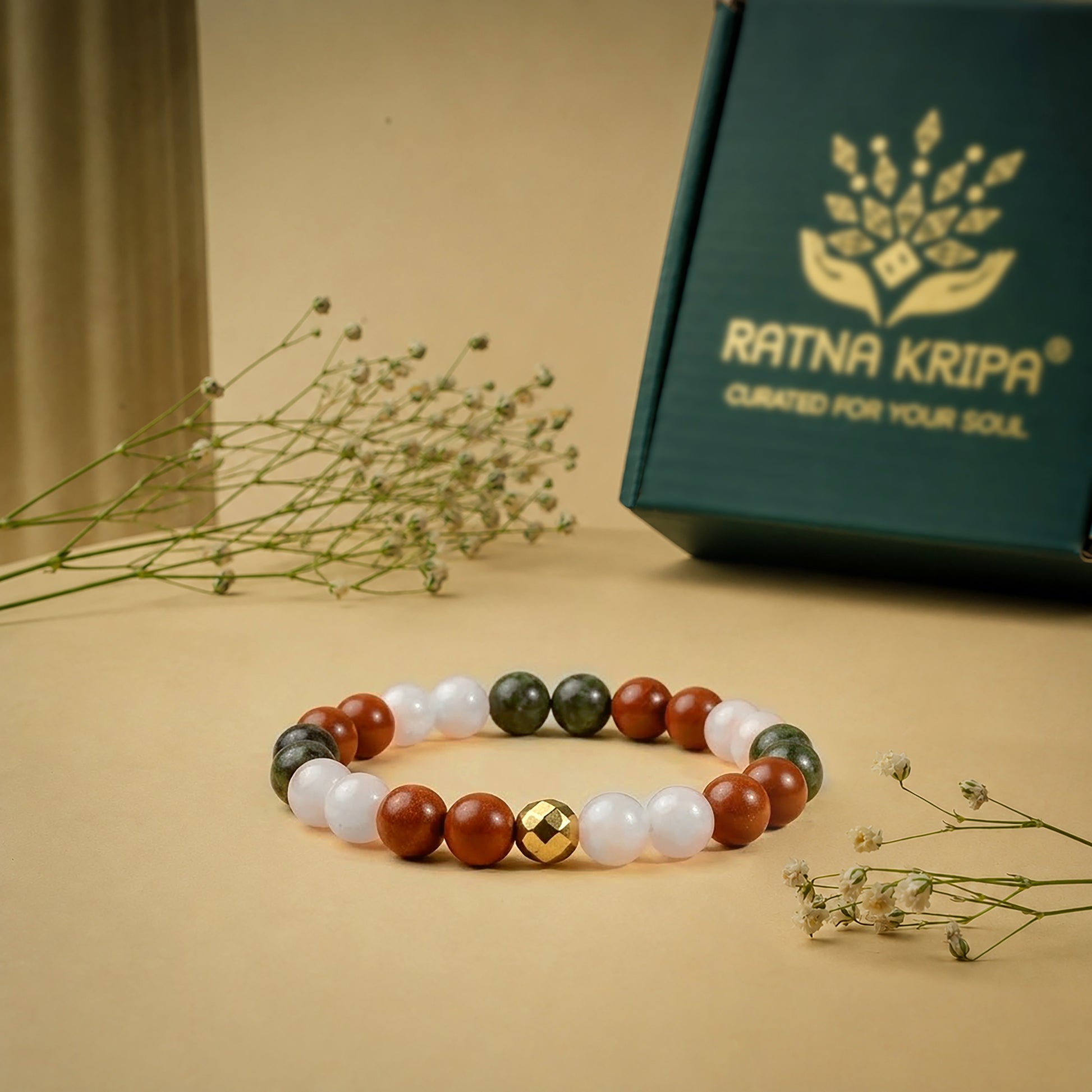 Beaded bracelet with a gold accent on a beige surface, next to a green box with 'Ratna Kripa' branding.