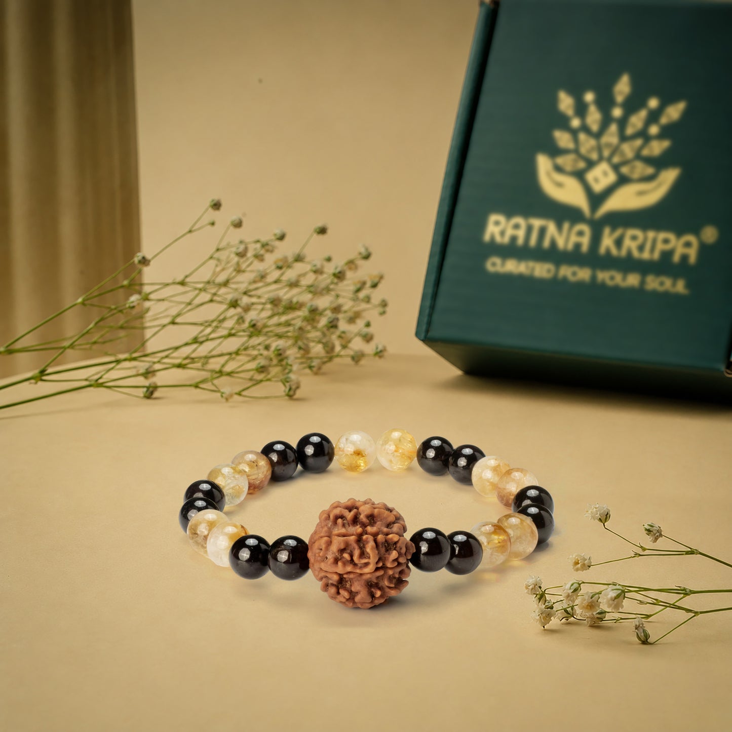 Bracelet with black, white, and brown beads on a beige surface with a 'Ratna Kripa' box in the background.