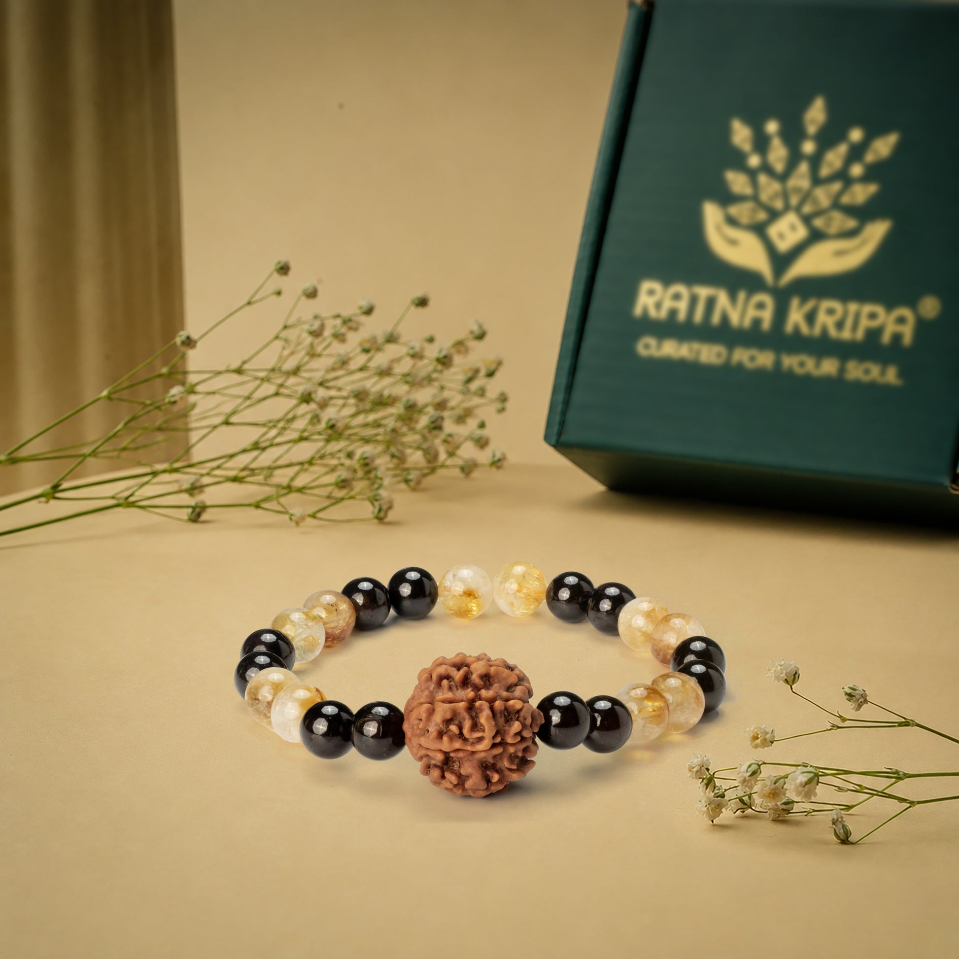 Bracelet with black, white, and brown beads on a beige surface with a 'Ratna Kripa' box in the background.